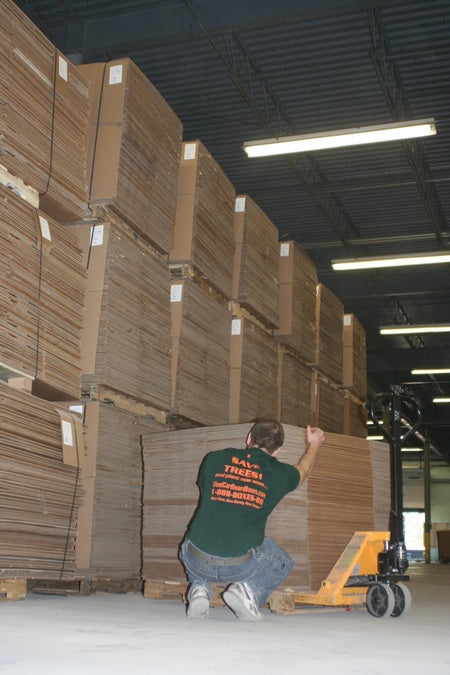 Zac Fratkin at UsedCardboardBoxes warehouse, in front of tens of thousands of used cardboard boxes, stacking used moving boxes after inspections for quality and integrity.